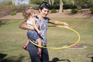 A volunteer holds a young girl while they hula hoop together.
