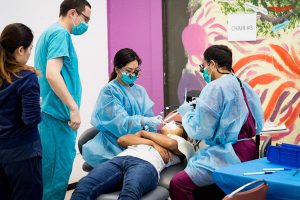 Three students provide dental care to the patient.